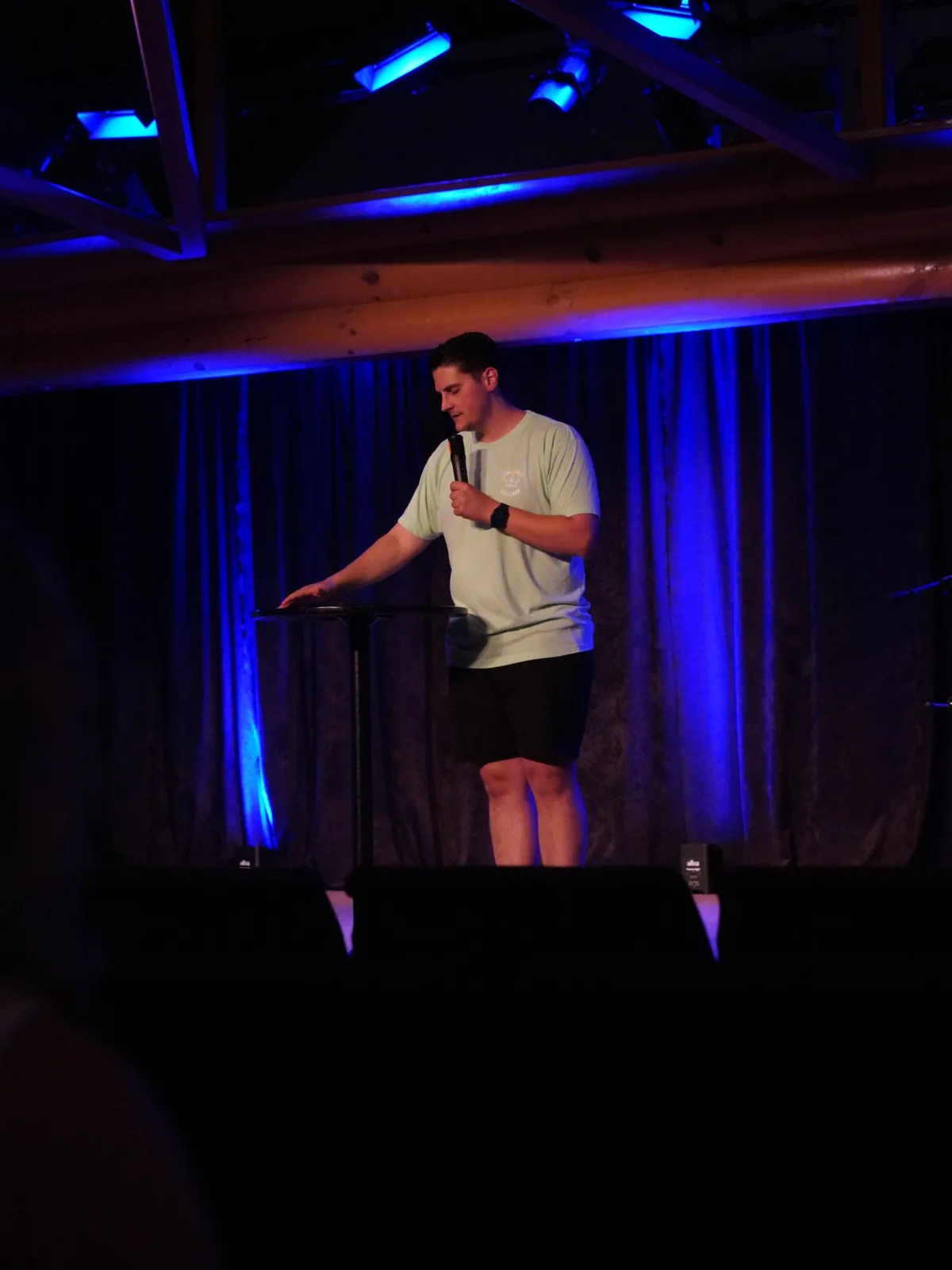 Carlo Orlando speaking on a camp stage lit in blue